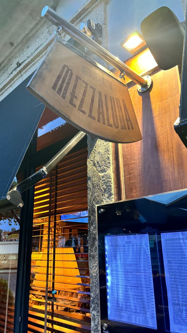 A restaurant sign reading MEZZALUNA is mounted above a menu display outside an establishment, with warm lighting and wooden accents visible