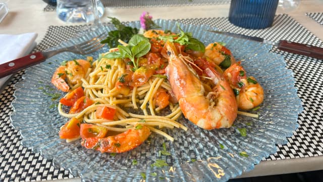 A plate of gluten free spaghetti with shrimp, cherry tomatoes, and fresh herbs, garnished with a sprig of basil