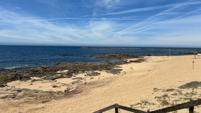 A sandy beach with scattered rocks, bordered by a calm blue sea under a sky with wispy clouds