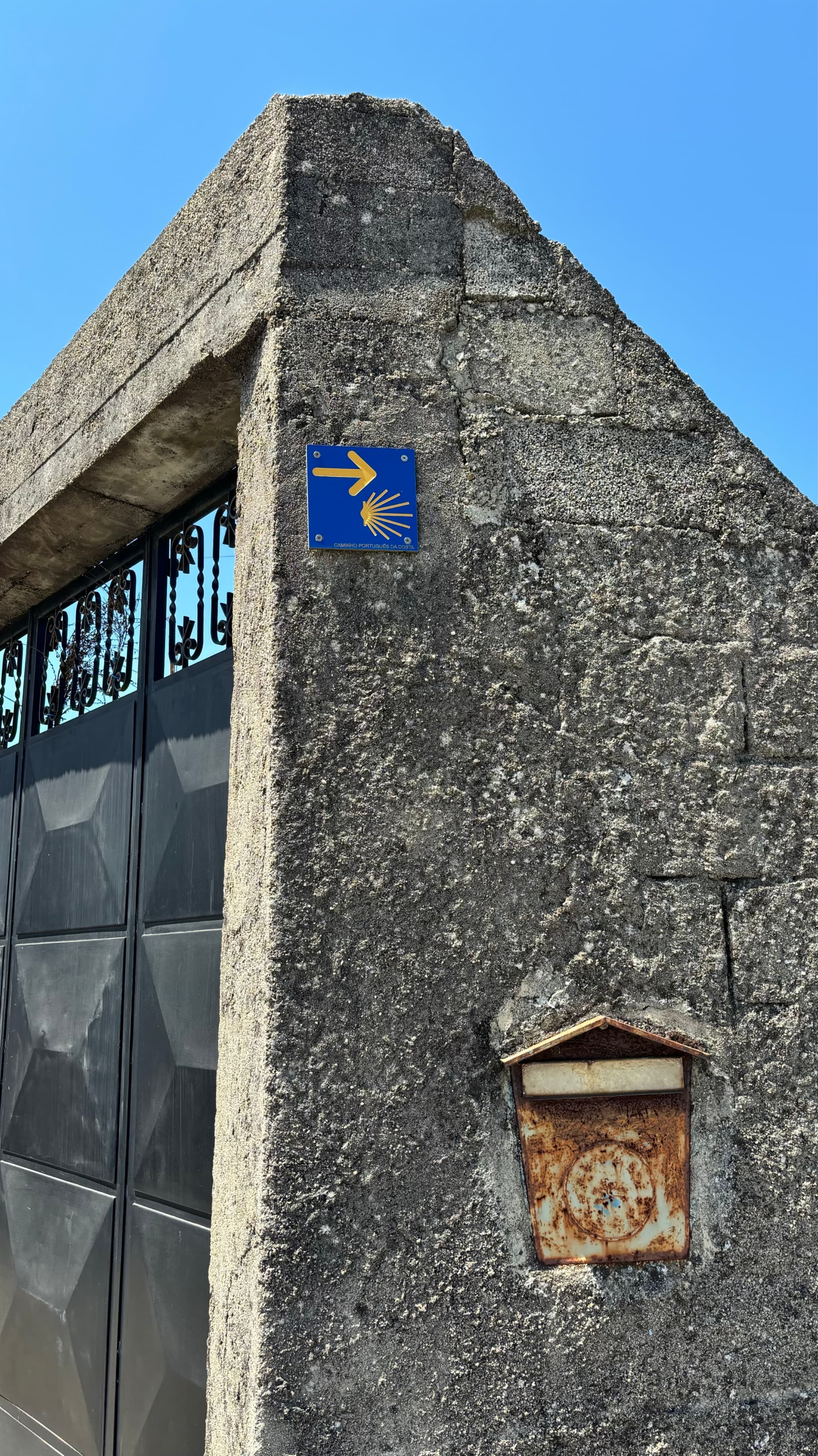A stone wall with a blue sign featuring a yellow arrow and shell symbol, next to a rusty mailbox
