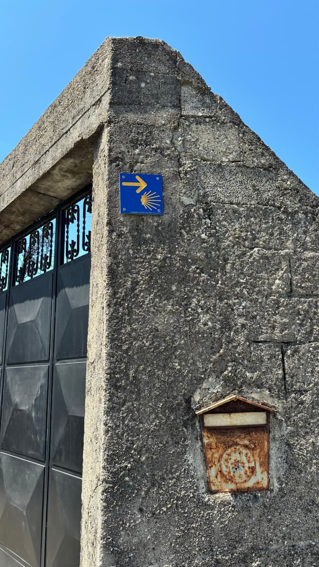 A stone wall with a blue sign featuring a yellow arrow and shell symbol, next to a rusty mailbox