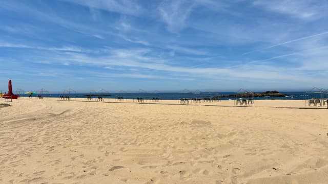 A sandy beach with a clear blue sky, a red lifeguard tower on the left, and the ocean in the background
