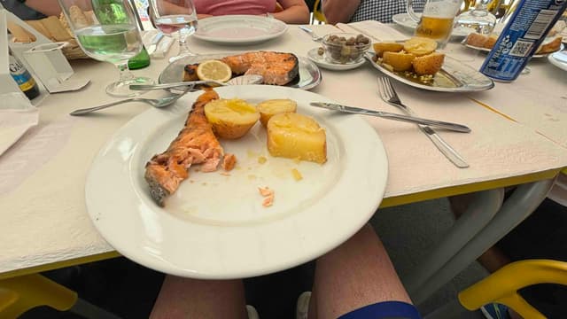 A plate with salmon and potatoes on a table set for a meal, surrounded by drinks and other dishes.