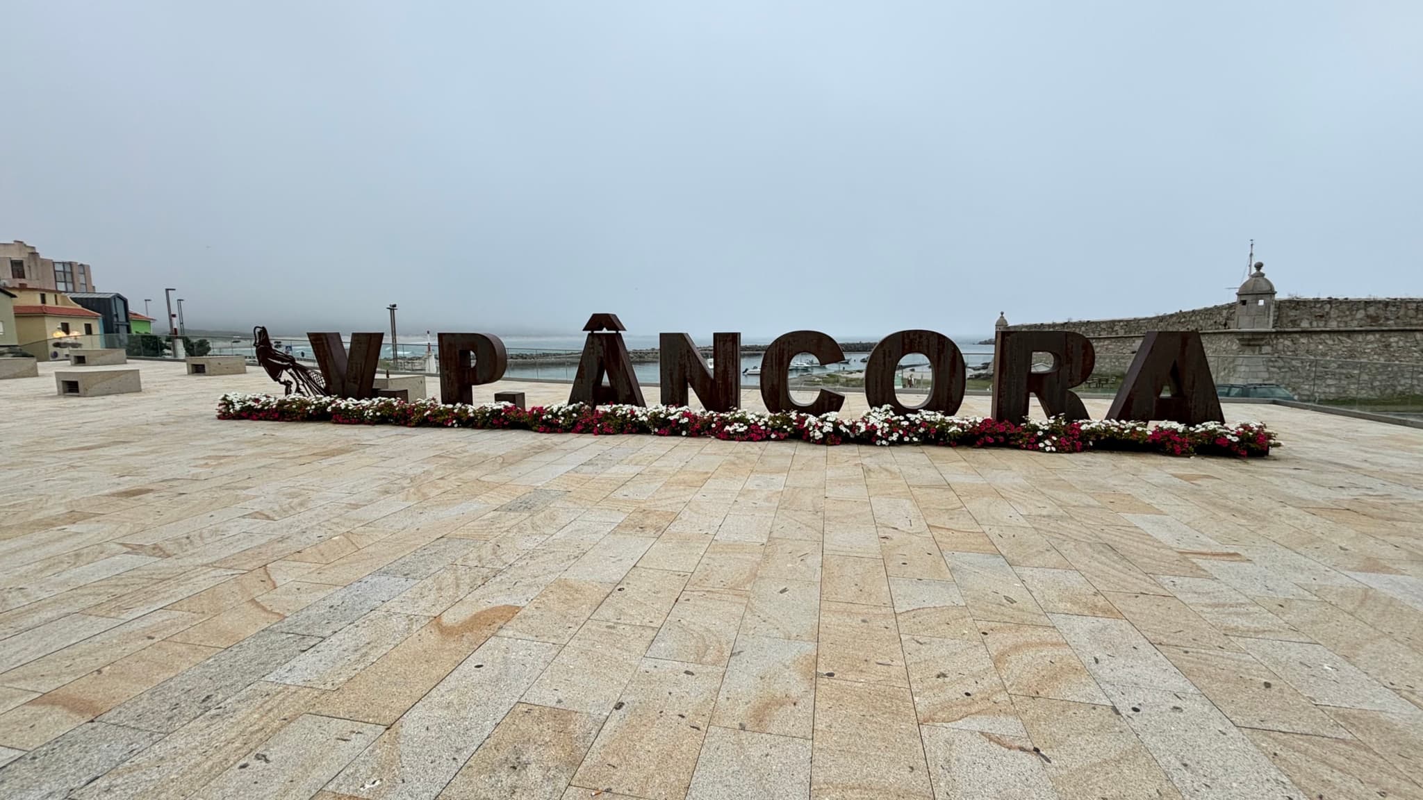 Large letters spelling V.P. ÂNCORA on a paved area, with a cloudy sky and buildings in the background