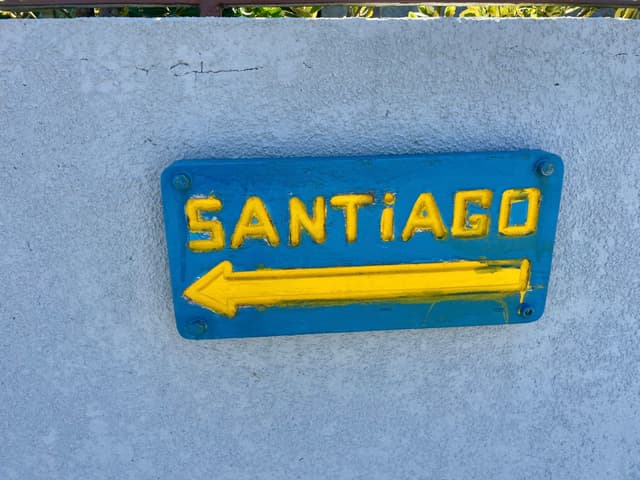 A blue sign with the word Santiago in yellow and a yellow arrow pointing left